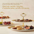 Two-tiered white ceramic serving stands with gold trim and gold metal handles, styled with assorted chocolates, grapes, macarons, and figs on a light beige background with promotional text.