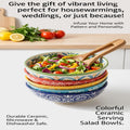 Set of colorful ceramic salad bowls with a wooden spoon on a kitchen counter, surrounded by fresh vegetables.