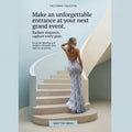 A woman stands on a curved staircase wearing a sleeveless, backless silver-gray evening gown with a tie at the back. The scene is set in a clean architectural interior with pale blue and beige tones, with promotional text reading 'THE EVENING COLLECTION' and 'Make an unforgettable entrance at your next grand event.