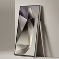 A sleek silver tablet or digital device with a large reflective screen, shown leaning against a light gray wall with a matching stylus beside it.