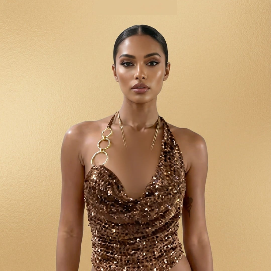 A model wearing a sparkling gold sequined halter dress stands against a textured gold background with the text 'DAZZLE. DEFINE.